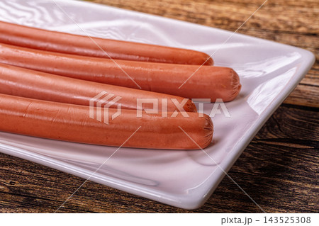 White rectangular ceramic plate holding four raw pink frankfurter sausages on rustic dark wood table surface food ingredient White rectangular ceramic plate holding four raw pink frankfurter sausages on rustic dark wood table surface food ingredient 143525308
