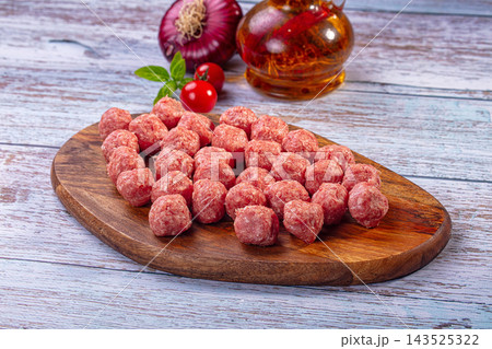 Wooden cutting board holding raw minced beef spheres alongside red onion and oil bottle on rustic table surface 143525322