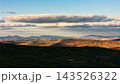 Sunlight highlights the textured surface of a grassy hill in the foreground. 143526322