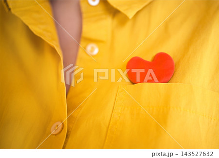 Close view of bright yellow collared shirt with visible buttons and red heart shaped object tucked into chest pocket, colorful clothing detail and symbolic accessory Close view of bright yellow collared shirt with visible buttons and red heart shaped object tucked into chest pocket, colorful clothing detail and symbolic accessory 143527632