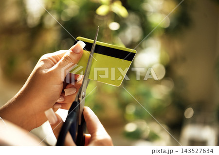 Hands cutting a blank yellow and black plastic card with scissors against softly blurred green foliage and warm sunlight, closeup household object scene Hands cutting a blank yellow and black plastic card with scissors against softly blurred green foliage and warm sunlight, closeup household object scene 143527634