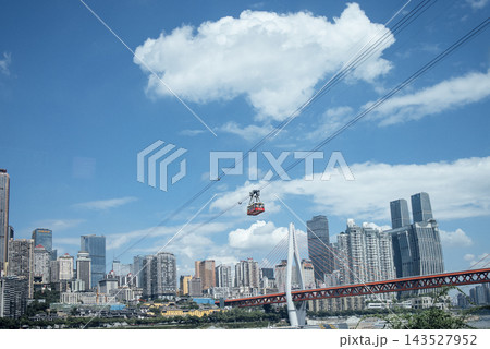 Cable car traveling over a cityscape with modern skyscrapers and a bridge under a blue sky with fluffy clouds in Chongqing, China Cable car traveling over a cityscape with modern skyscrapers and a bridge under a blue sky with fluffy clouds in Chongqing, China 143527952