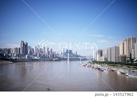Urban skyline of Chongqing, China, featuring modern skyscrapers along the Yangtze River with a clear blue sky and boats docked along the waterfront Urban skyline of Chongqing, China, featuring modern skyscrapers along the Yangtze River with a clear blue sky and boats docked along the waterfront 143527962
