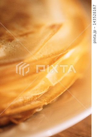 Close-up view of stacked golden pancakes on a white plate, showcasing texture and layers, with a blurred wooden background enhancing the food presentation 143528167