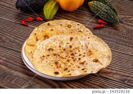 Freshly toasted flatbreads with charred golden spots stacked on white plate surrounded by avocado, peppers and chillies on rustic wood, healthy homemade food Freshly toasted flatbreads with charred golden spots stacked on white plate surrounded by avocado, peppers and chillies on rustic wood, healthy homemade food 143529138