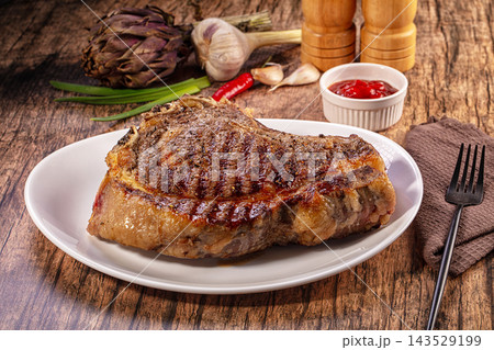 Grilled beef steak on white plate with garlic artichoke and red sauce on wooden table Grilled beef steak on white plate with garlic artichoke and red sauce on wooden table 143529199