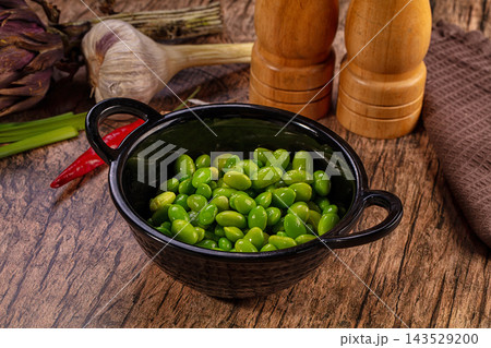 Green edamame soybeans in black ceramic bowl with garlic and pepper on wooden table, healthy snack food 143529200