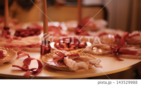 Elegant table setting with decorative plates, candles, and red ribbons for a festive occasion, featuring an inviting and warm atmosphere in a cozy indoor space 143529988