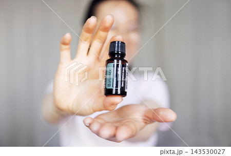 Woman holding essential oil bottle labeled Balance, showcasing natural wellness concept, with soft background emphasizing tranquility and holistic health benefits Woman holding essential oil bottle labeled Balance, showcasing natural wellness concept, with soft background emphasizing tranquility and holistic health benefits 143530027