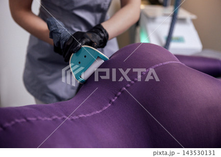 Female technician in gray uniform using a roller on a purple fabric surface, showcasing the process of upholstery repair and restoration in a modern workspace Female technician in gray uniform using a roller on a purple fabric surface, showcasing the process of upholstery repair and restoration in a modern workspace 143530131