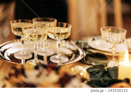 Elegant glassware filled with sparkling beverage arranged on a silver tray, surrounded by festive table settings, creating a warm and inviting atmosphere for celebration 143530133