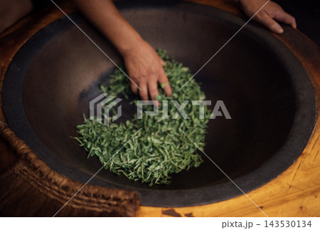 Hand of a person sorting fresh green tea in a large wooden bowl, showcasing the intricate process of preparing natural ingredients for culinary or medicinal use 143530134