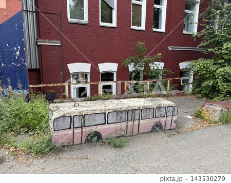 Abandoned pink bus bench beside overgrown courtyard and red brick building with windows and graffiti wall 143530279