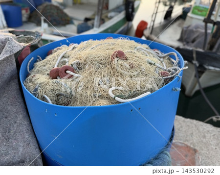 Fishing net tangled in blue storage container aboard working vessel with maritime equipment in background Fishing net tangled in blue storage container aboard working vessel with maritime equipment in background 143530292