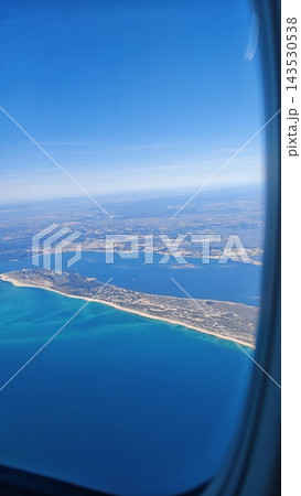Aerial view of turquoise coastline, sandy peninsula, urban shoreline, blue sea and distant horizon through an airplane window over a coastal landscape Aerial view of turquoise coastline, sandy peninsula, urban shoreline, blue sea and distant horizon through an airplane window over a coastal landscape 143530538