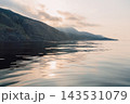 Warm sunset light reflects on sea creating a serene landscape with dramatic hills and open water. 143531079
