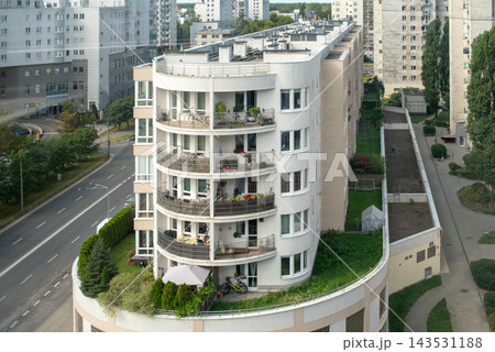 Residents use balconies and a rooftop garden in a curved urban apartment building. Urban living, community, sustainability, balcony garden, family life, modern housing. 143531188