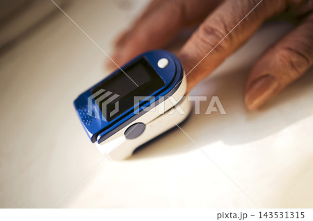 Fingertip pulse oximeter with dark display beside an older hand on a light surface, showing compact medical monitoring device in closeup 143531315
