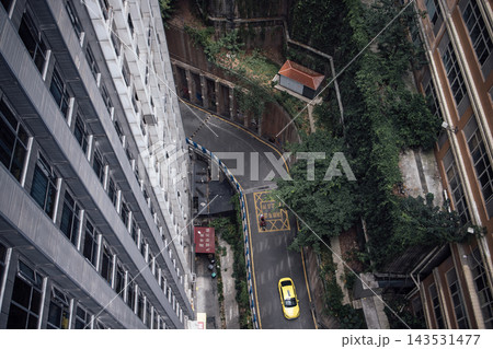 Aerial view of a yellow taxi navigating a winding road between tall buildings and greenery in an urban setting, showcasing a mix of architecture and nature Aerial view of a yellow taxi navigating a winding road between tall buildings and greenery in an urban setting, showcasing a mix of architecture and nature 143531477