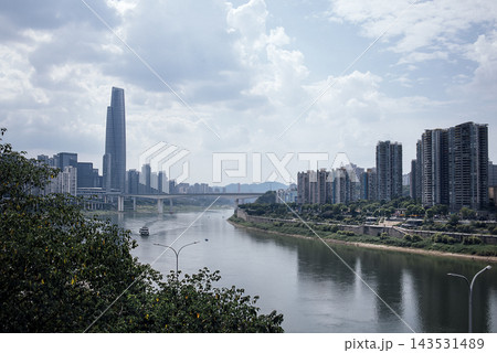 Urban skyline of Chongqing, China featuring modern skyscrapers, a river, and a bridge under a cloudy sky with lush greenery in the foreground Urban skyline of Chongqing, China featuring modern skyscrapers, a river, and a bridge under a cloudy sky with lush greenery in the foreground 143531489