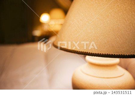 Warmly illuminated table lamp with textured beige shade and ceramic base beside blurred matching lamps in a softly lit indoor setting Warmly illuminated table lamp with textured beige shade and ceramic base beside blurred matching lamps in a softly lit indoor setting 143531511