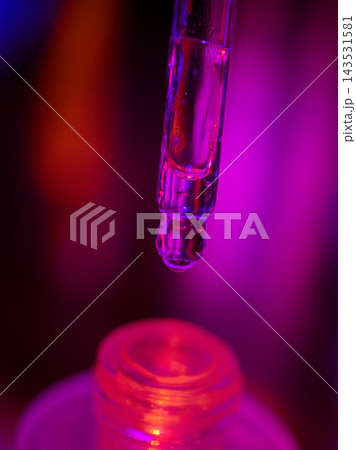 Transparent laboratory test tube suspended above a small glass container with vivid magenta and red lighting, close up abstract scientific glassware composition Transparent laboratory test tube suspended above a small glass container with vivid magenta and red lighting, close up abstract scientific glassware composition 143531581