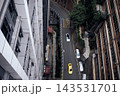 Aerial view of urban street with two cars navigating a winding road surrounded by tall buildings and greenery in a city environment 143531701