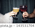 Two hands holding cocktails, one with a yellow drink in a coupe glass and the other with a purple drink in a stemmed glass against a dark background 143531704