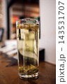 Transparent glass filled with herbal tea and floating leaves on wooden table, soft background with blurred elements creating a warm atmosphere 143531707