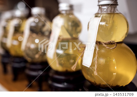 Decorative glass bottles filled with herbal infusion displayed on wooden stand, featuring labels and twine accents, arranged in a row for aesthetic presentation Decorative glass bottles filled with herbal infusion displayed on wooden stand, featuring labels and twine accents, arranged in a row for aesthetic presentation 143531709