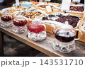 Glass teapots filled with colorful herbal tea displayed on a wooden table alongside various dried fruits and herbs in a market setting 143531710
