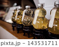 Decorative glass bottles filled with yellow liquid displayed on wooden shelf with black stands in a modern interior setting, labels attached for identification 143531711