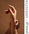 Close-up of two human hands intertwined against a soft brown background, showcasing delicate fingers and natural skin tones in a serene composition 143531714
