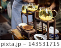 Glass teapots filled with herbal tea and lemon slices displayed on wooden shelves in a tea shop, with various tea leaves visible in the background 143531715