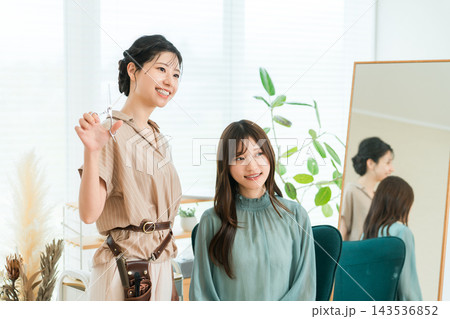 美容室でお客様のヘアカットを担当する笑顔の女性美容師。ヘアサロンの接客イメージ 美容室でお客様のヘアカットを担当する笑顔の女性美容師。ヘアサロンの接客イメージ 143536852