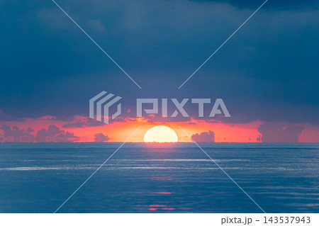 A stunning view of the sun setting over the calm ocean horizon, casting a radiant glow across the water and illuminating dramatic clouds with fiery red and orange hues. A stunning view of the sun setting over the calm ocean horizon, casting a radiant glow across the water and illuminating dramatic clouds with fiery red and orange hues. 143537943