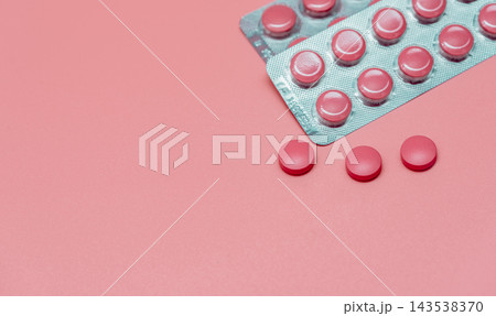 Pink round tablets in silver blister packs beside three loose pills on a pink surface, oral pharmaceutical products with clear plastic pockets for women's health and vitamin supplement communication. Pink round tablets in silver blister packs beside three loose pills on a pink surface, oral pharmaceutical products with clear plastic pockets for women's health and vitamin supplement communication. 143538370