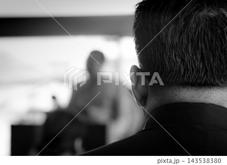 Man wearing a black shirt listening to a monk delivering a sermon at a Buddhist funeral in Thailand, attending a traditional religious ceremony. 143538380