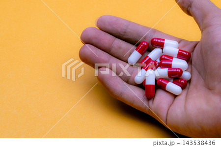 Man holding a handful of red and white prescription capsules in his palm over a yellow surface, oral medication associated with drug overdose awareness, toxicity risks and safer medication use. 143538436