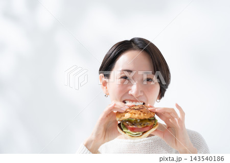 美味しいハンバーガーを食べる笑顔の女性 美味しいハンバーガーを食べる笑顔の女性 143540186