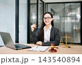 Asian female lawyer in a suit and glasses sitting at her modern office desk. Professional attorney providing trusted legal advice 143540894