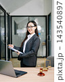 Asian female lawyer in a suit holding a contract in her office. Confident attorney standing by a desk 143540897