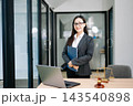 Asian female lawyer in a suit holding a contract in her office. Confident attorney standing by a desk 143540898