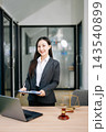 Asian female lawyer in a suit holding a contract in her office. Confident attorney standing by a desk 143540899