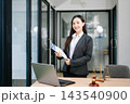 Asian female lawyer in a suit holding a contract in her office. Confident attorney standing by a desk 143540900