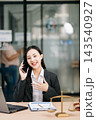 Asian female lawyer talking on a smartphone at her modern office desk. Confident attorney giving legal advice near a laptop, gavel 143540927