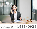 Asian female lawyer talking on a smartphone at her modern office desk. Confident attorney giving legal advice near a laptop, gavel 143540928