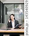 Asian female lawyer talking on a smartphone at her modern office desk. Confident attorney giving legal advice near a laptop, gavel 143540929