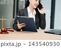 Asian female lawyer talking on a smartphone at her modern office desk. Confident attorney giving legal advice near a laptop, gavel 143540930