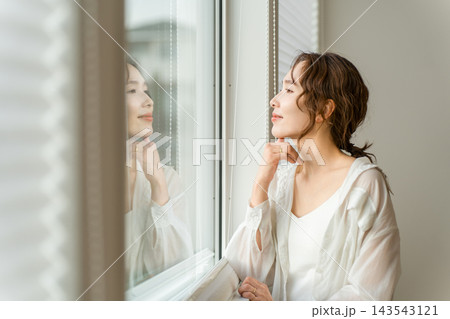 家のリビングの窓辺で外を眺めながらくつろぐ女性。穏やかな暮らしのひととき 143543121
